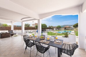 An outdoor patio with a dining table, chairs, and a view of a swimming pool and greenery.