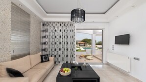 Un salón moderno con un sofá, una mesa de centro con fruta, una lámpara de araña y vistas a una piscina.