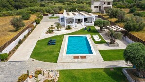 Una villa moderna con piscina, rodeada por un césped y jardín bien cuidados.