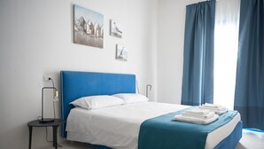 A bedroom with a bed, a nightstand, a lamp, and a window with curtains. - Cala Moresca in Golfo Aranci (Golfo Aranci)