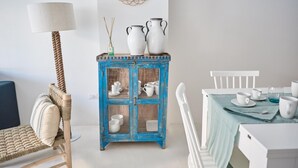 A dining area with a blue cabinet containing white dishes, a white chair, and a table with a light blue tablecloth. - Cala Moresca in Golfo Aranci (Golfo Aranci)