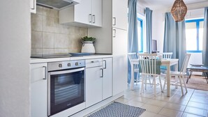 A modern kitchen with white cabinetry, a built-in oven, and a dining area with a table and chairs. - Marinella in Golfo Aranci (Golfo Aranci)