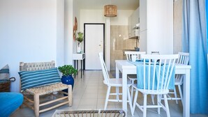 A modern apartment with a dining area, a living room with a sofa and a chair, and a kitchen visible through an open door. - Marinella in Golfo Aranci (Golfo Aranci)