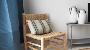 A wicker chair with a striped cushion, a metal table with two white vases, and a blue curtain. - Spiaggia del Principe (Arzachena)