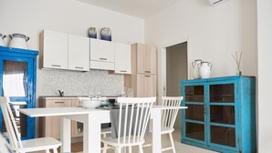 A modern kitchen with white cabinets, a dining table with chairs, and a blue cabinet with glass doors.