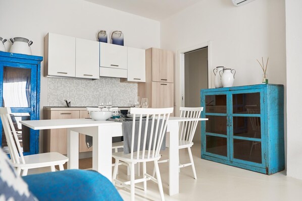 A modern kitchen with white cabinets, a dining table with chairs, and a blue cabinet with glass doors.