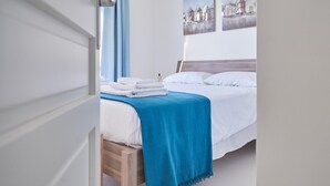 A neatly made bed with white linens and a blue blanket, a wooden headboard, and a wall with two paintings. - Cala Coticcio in Golfo Aranci (Golfo Aranci)