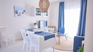 A modern dining area with white furniture, a large woven light fixture, and a view of a blue ocean through sheer curtains. - Cala Coticcio in Golfo Aranci (Golfo Aranci)