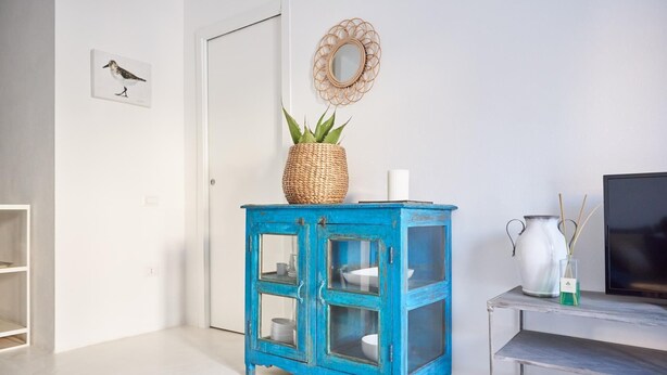 A room with a blue cabinet with glass doors, a wicker basket with a plant, a white vase, and a television on a stand. - Cala Sabina in Golfo Aranci (Golfo Aranci)
