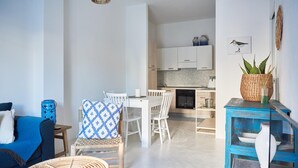 A modern living room with a blue sofa, a dining area with white chairs, and a kitchen with white cabinets. - Cala Sabina in Golfo Aranci (Golfo Aranci)