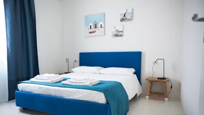 A modern bedroom with a blue bed, white linens, and a blue headboard. There are two bedside tables with lamps, and artwork on the wall. - Cala Sabina in Golfo Aranci (Golfo Aranci)