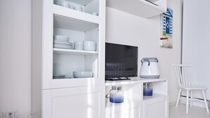 Une cuisine moderne avec des meubles blancs, un téléviseur à écran plat et une bouilloire.