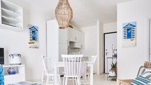 Une pièce moderne et bien éclairée, avec un coin repas, des meubles blancs et une cuisine à l’arrière-plan.