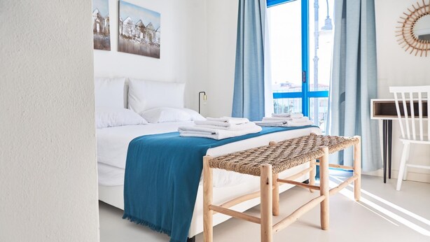 Une chambre à coucher avec un lit, un banc, un bureau et une fenêtre avec des rideaux.