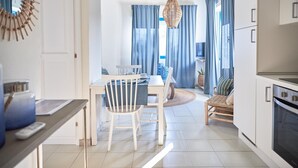 A modern kitchen with white cabinetry, a dining area with a white table and chairs, and a living area with a sofa and curtains. - Liscia Ruja in Golfo Aranci (Golfo Aranci)