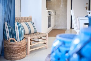 A room with a wicker chair, striped pillows, a woven basket, and a kitchen area in the background. - Liscia Ruja in Golfo Aranci (Golfo Aranci)