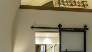 A hotel room with a bed, a bedside table with a lamp, a mirror, a bathroom with a sink and a shower, and a sliding door. - KerkHotel Biervliet (Biervliet)