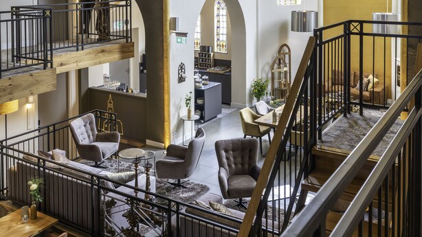 A spacious interior with high ceilings, arched windows, and a mezzanine level with seating. - KerkHotel Biervliet (Biervliet)