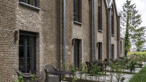 A brick building with large windows and a patio area with outdoor furniture. - KerkHotel Biervliet (Biervliet)