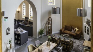 A spacious interior with high vaulted ceilings, stained glass windows, and a mix of seating areas including a dining table and sofas. - KerkHotel Biervliet (Biervliet)