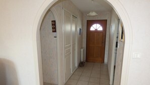 Un pasillo con suelo de baldosas, una puerta de madera al final y una pared blanca con una lámpara.
