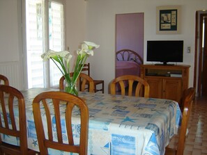 A dining area with a table set for four, a television on a wooden cabinet, and a vase with flowers on the table.