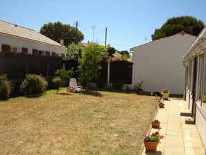 A residential backyard with a lawn, potted plants, a chair, and a dog.