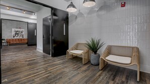 A modern lobby with a wooden floor, two wicker sofas with cushions, a potted plant, and pendant lighting.
