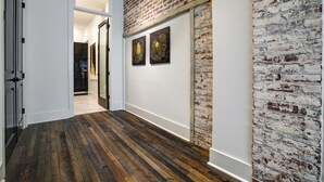 A hallway with a wooden floor, white walls, and a brick accent wall. There are two framed artworks on the brick wall.
