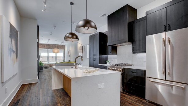 A modern kitchen with a central island, stainless steel appliances, dark cabinetry, and pendant lighting.
