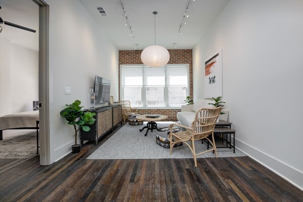 A modern living room with a sofa, chairs, a coffee table, and a TV. There is a large window with a view of the outside.