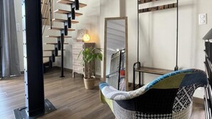 A modern interior with a wooden staircase, a hanging light fixture, a mirror, and a patterned chair.