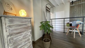 A modern interior with a rustic wooden dresser, a potted plant, a metal chair, and a staircase leading to another level.