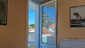 A room with a bed, a sliding glass door leading to a balcony, a framed picture on the wall, and a small white cabinet.