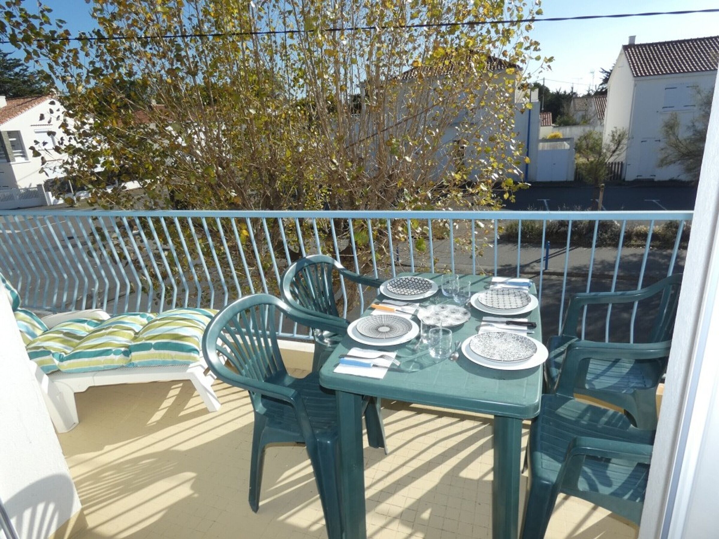 Un balcón con mesa lista para comer, rodeado de sillas de plástico verde.