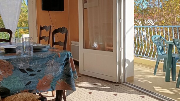A balcony with a table set for dining, chairs, and a television mounted on the wall.