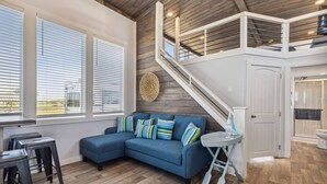 Een moderne woonkamer met een blauwe hoekbank, houten vloeren, een trap en uitzicht op het buitengebied.