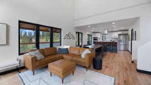 A spacious living room with a large sectional sofa, a dining area with a long table, and a kitchen with modern appliances.