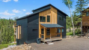 A modern two-story cabin with a wooden exterior, a balcony, and a view of a forested area.