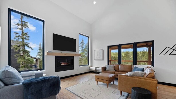 A modern living room with a fireplace, large windows, and a flat-screen TV.