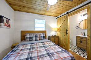 Un dormitorio con edredón a cuadros, cabecero de madera, una mesita de noche, un armario de madera y una ventana con persianas.