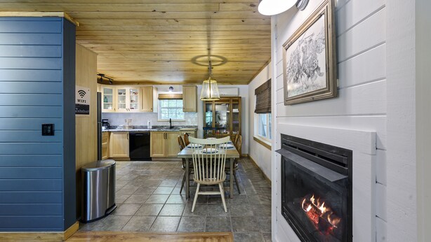 A modern kitchen with a fireplace, wooden ceiling, and a dining area with a table and chairs. - Welcome Bow- 6 guest/Hot Tub/Location (Broken Bow)