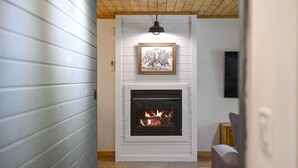 A modern fireplace with a framed picture above it, a wooden ceiling, and a TV mounted on the wall. - Welcome Bow- 6 guest/Hot Tub/Location (Broken Bow)
