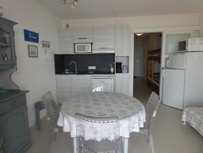 Una cocina compacta con microondas, cafetera y refrigerador. Hay una mesa de comedor con sillas y mantel estampado.