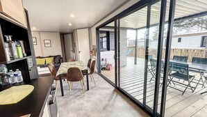 Ein geräumiges Zimmer mit einer großen Schiebeglasdoor, die auf eine Terrasse im Freien führt. Innenbereich mit Essbereich inklusive Tisch und Stühlen sowie einer Küchenzeile mit Arbeitsfläche und Schränken.