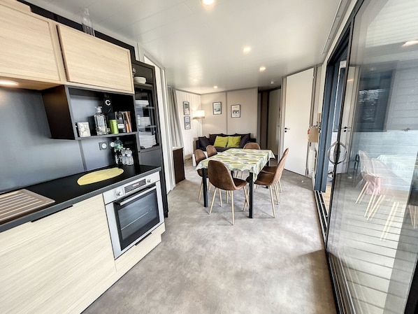 A compact kitchen with modern appliances, a dining area with a table and chairs, and a view through a glass door to an outdoor area.