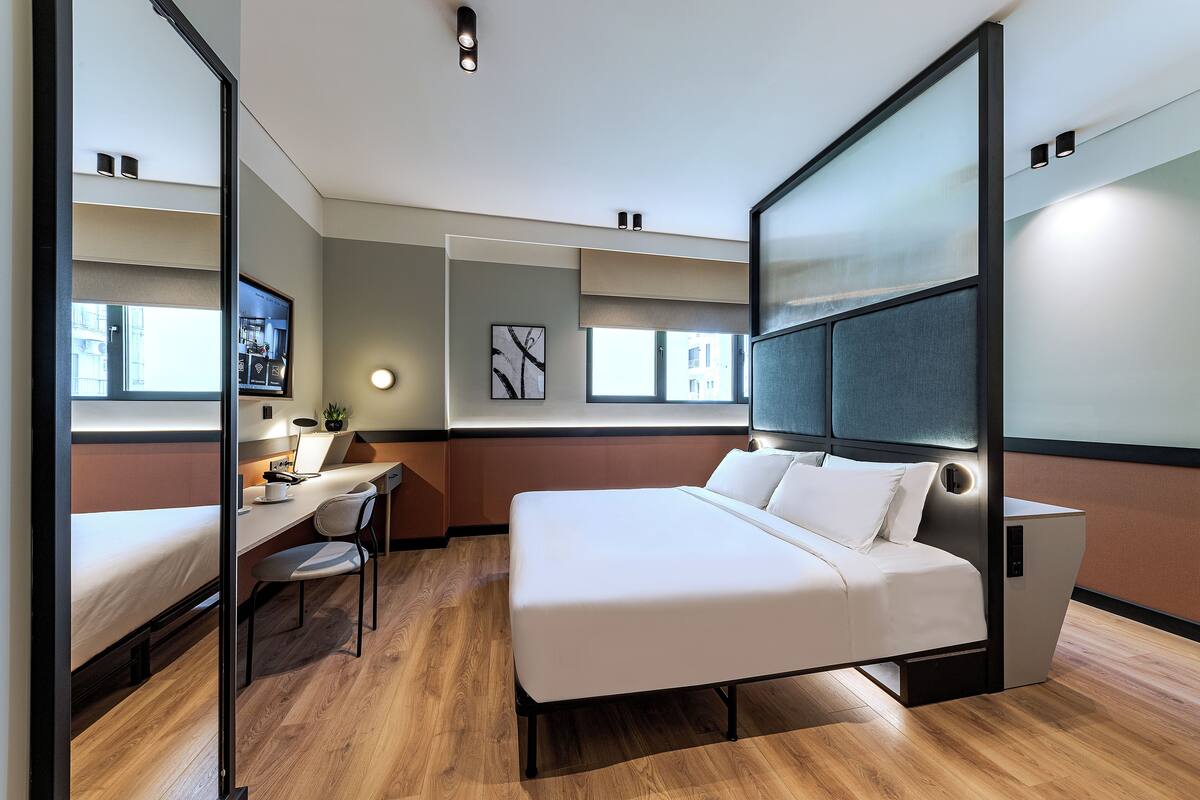 Moderni hotellihuone, jossa on sänky, työpöytä, tuoli ja suuri ikkuna.