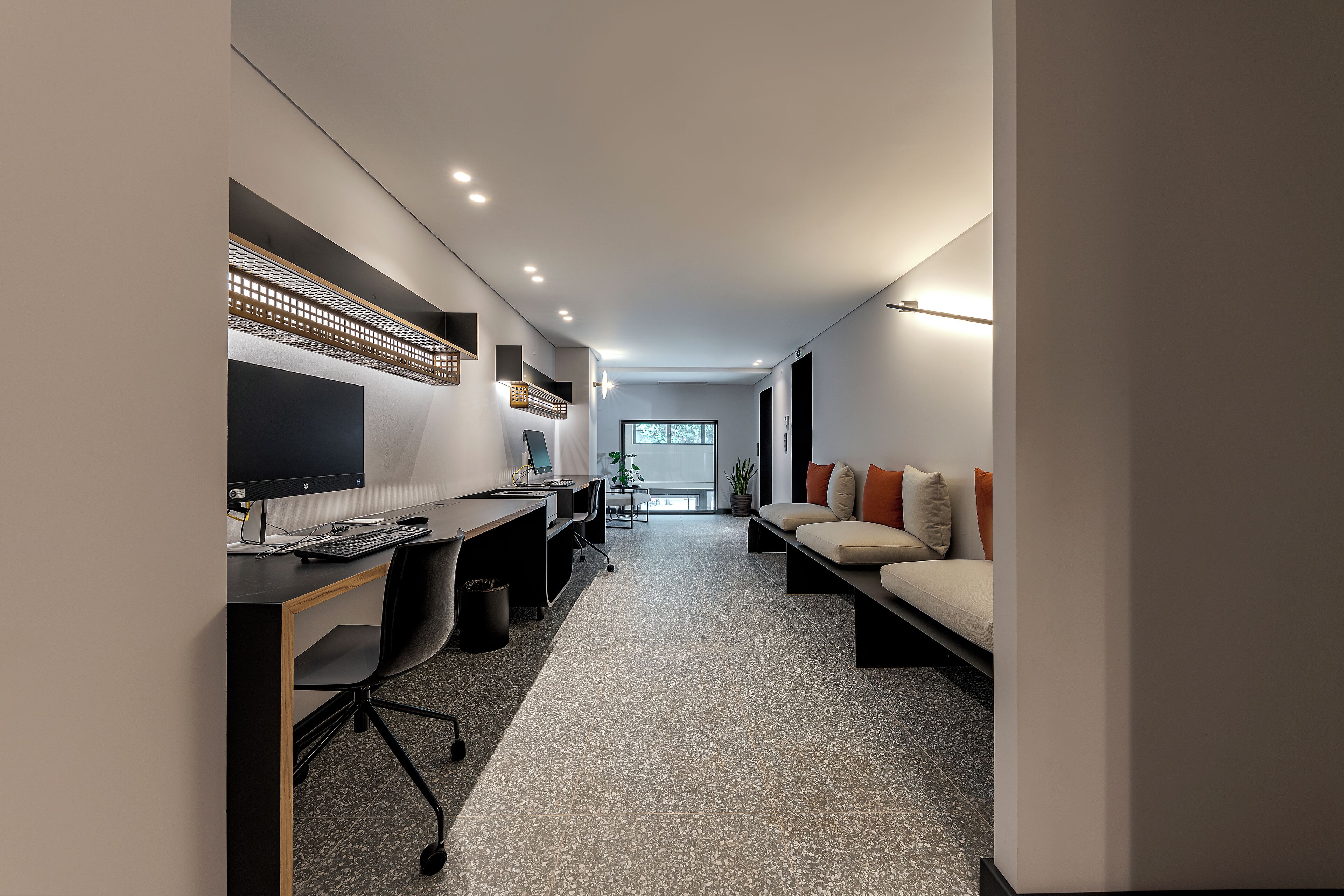 Un espacio de oficina moderno con escritorio, computadora y silla, un sofá con cojines, y una escalera que lleva a otra habitación.