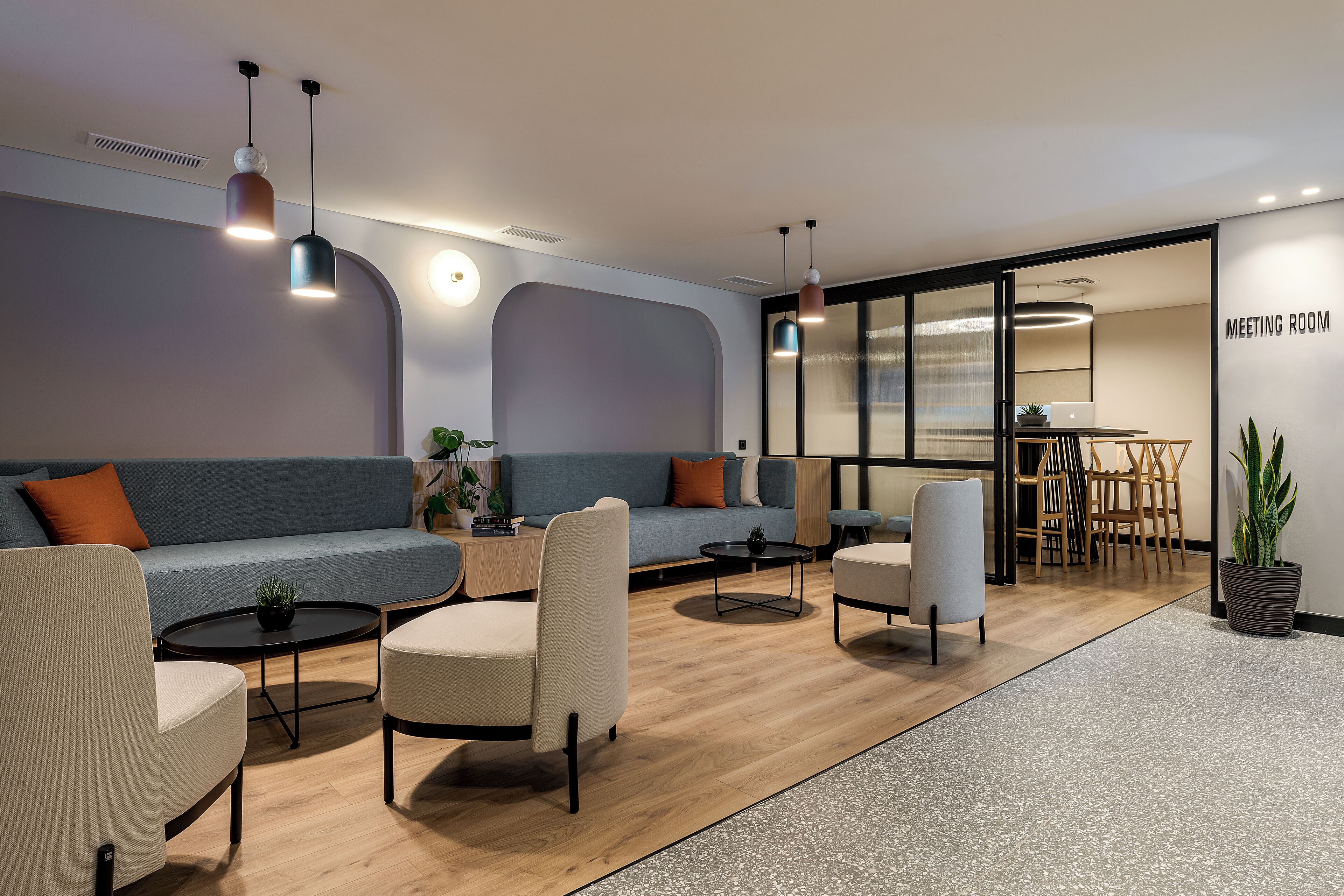 A modern meeting room with a sofa, chairs, a coffee table, and pendant lighting.