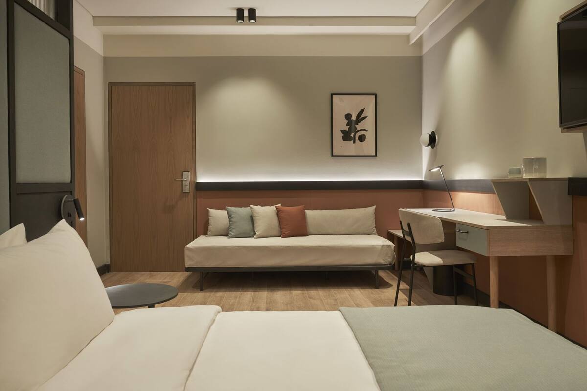 Moderni hotellihuone, jossa on sänky, työpöytä, tuoli, sohva ja ovi.